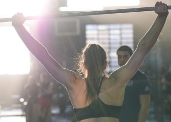 Crossfit athlete, seen from behind, trains with the barbell